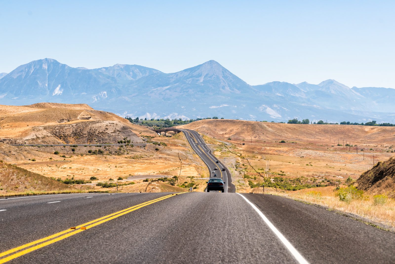 Open highway crossing dry hills toward distant mountains